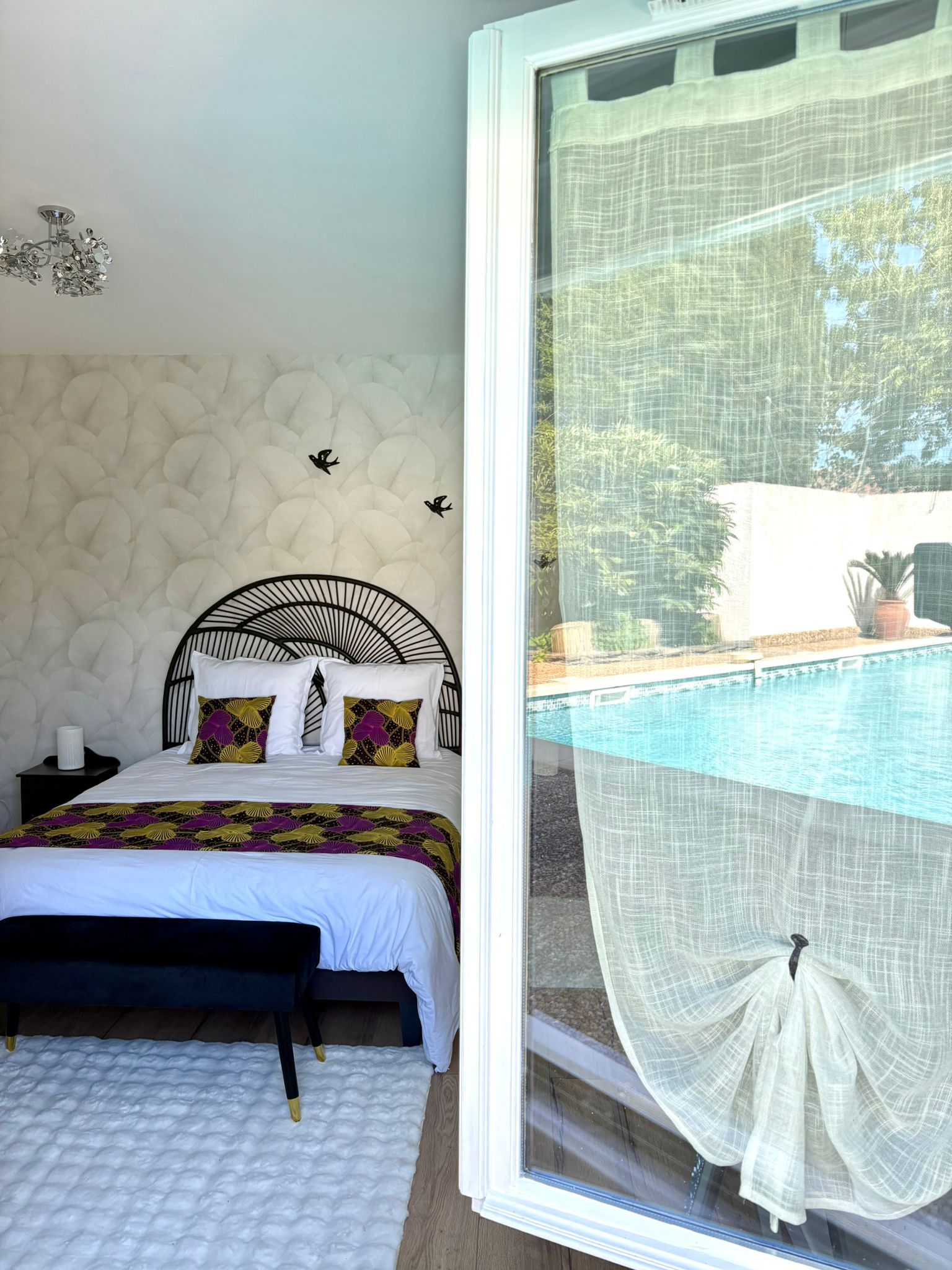 Un dormitorio con cama, mesita de noche, decoración en la pared y ventana con vista a una piscina.