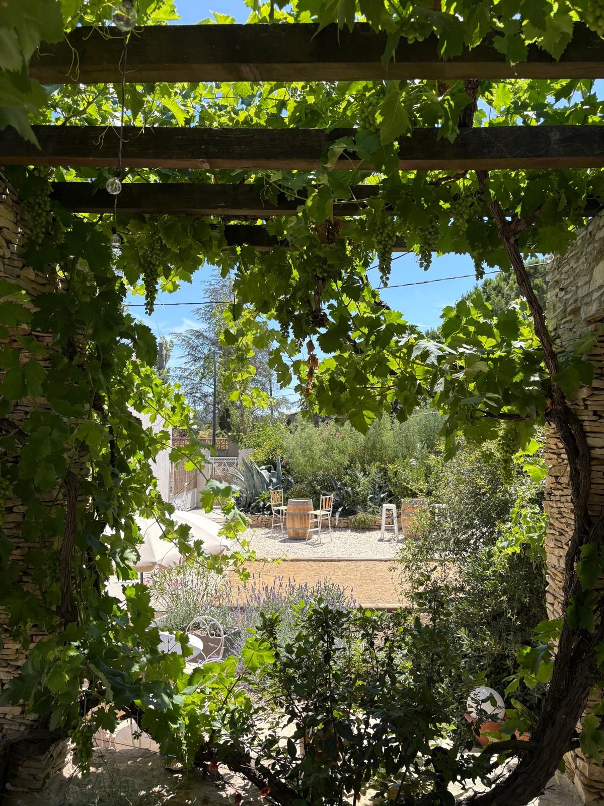 Un jardin agrémenté d’une pergola, d’un mur en pierre et d’un espace détente avec des chaises et une table.