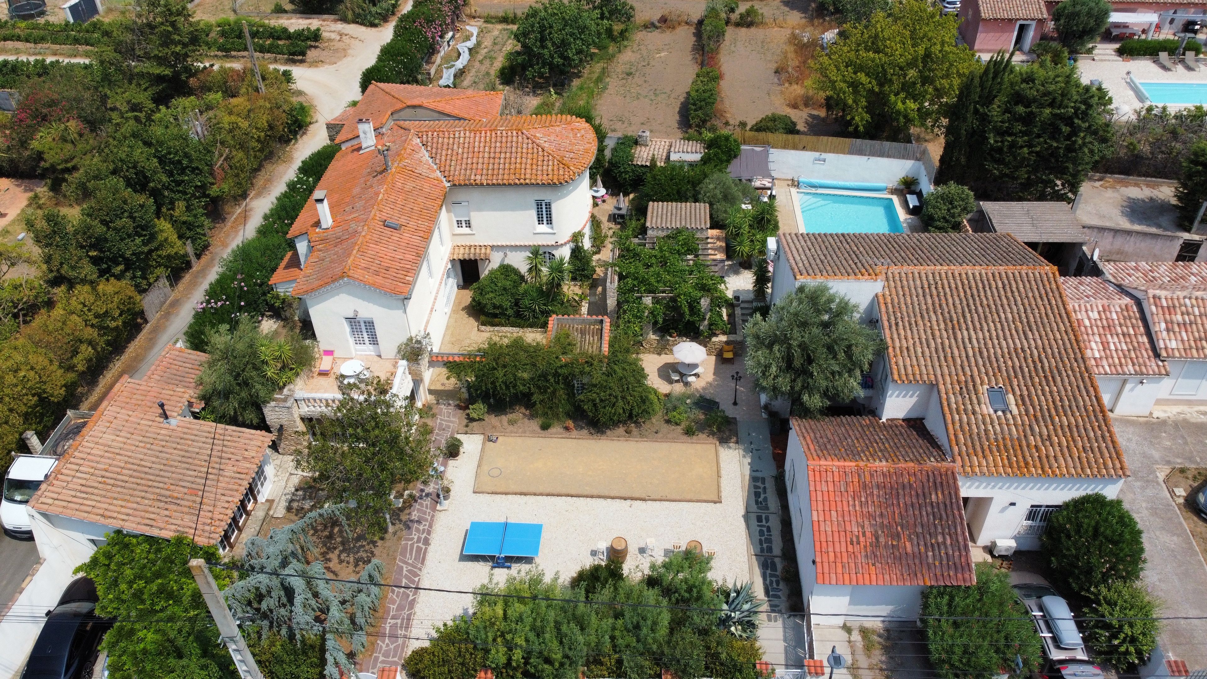 A residential area with houses featuring red-tiled roofs, a swimming pool, and a paved driveway.