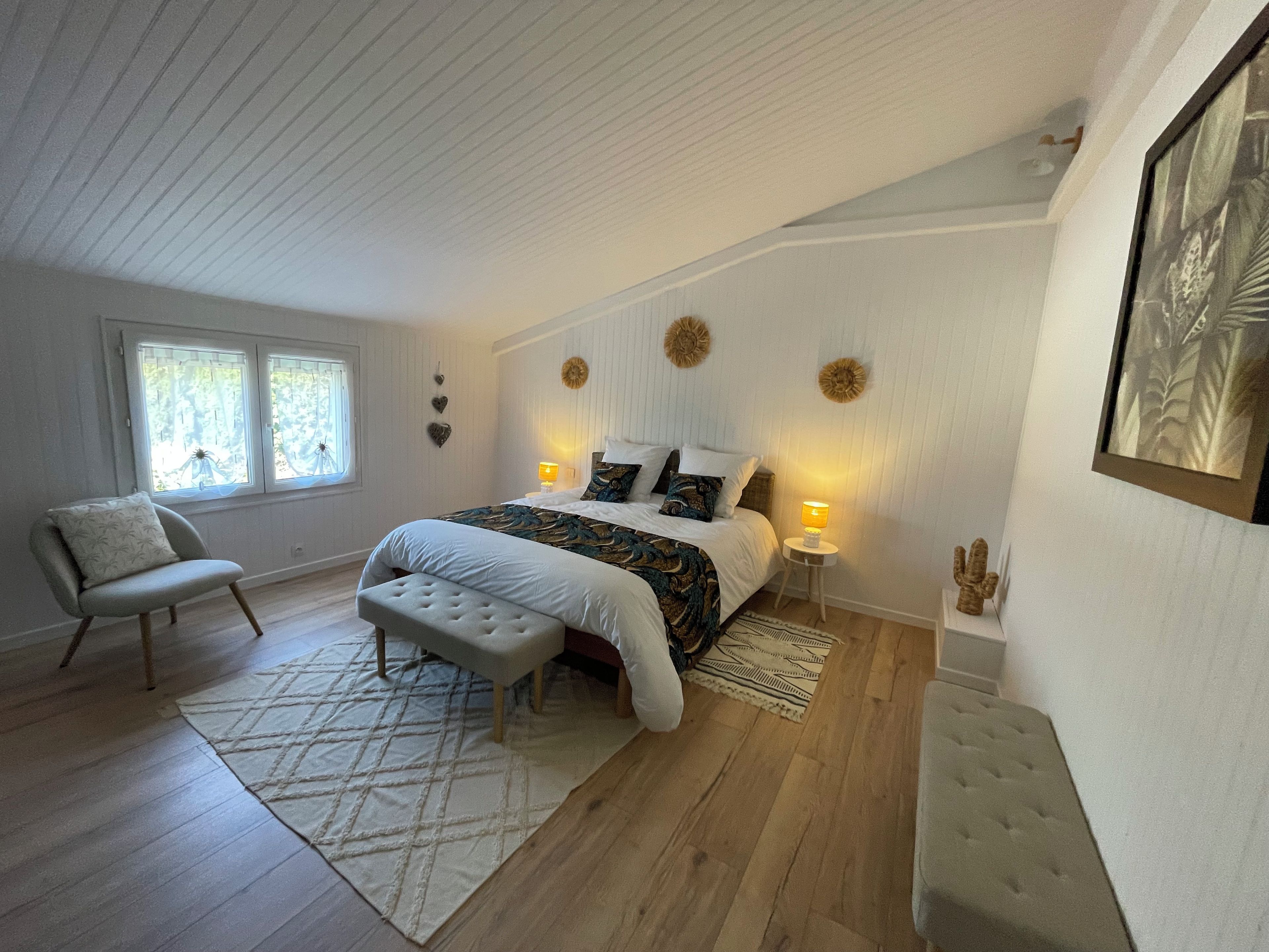 A bedroom with a large bed, a chair, a small table, and a window.