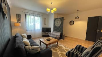 Una sala de estar con sofá, sillón, mesa de centro, televisor y decoración mural.