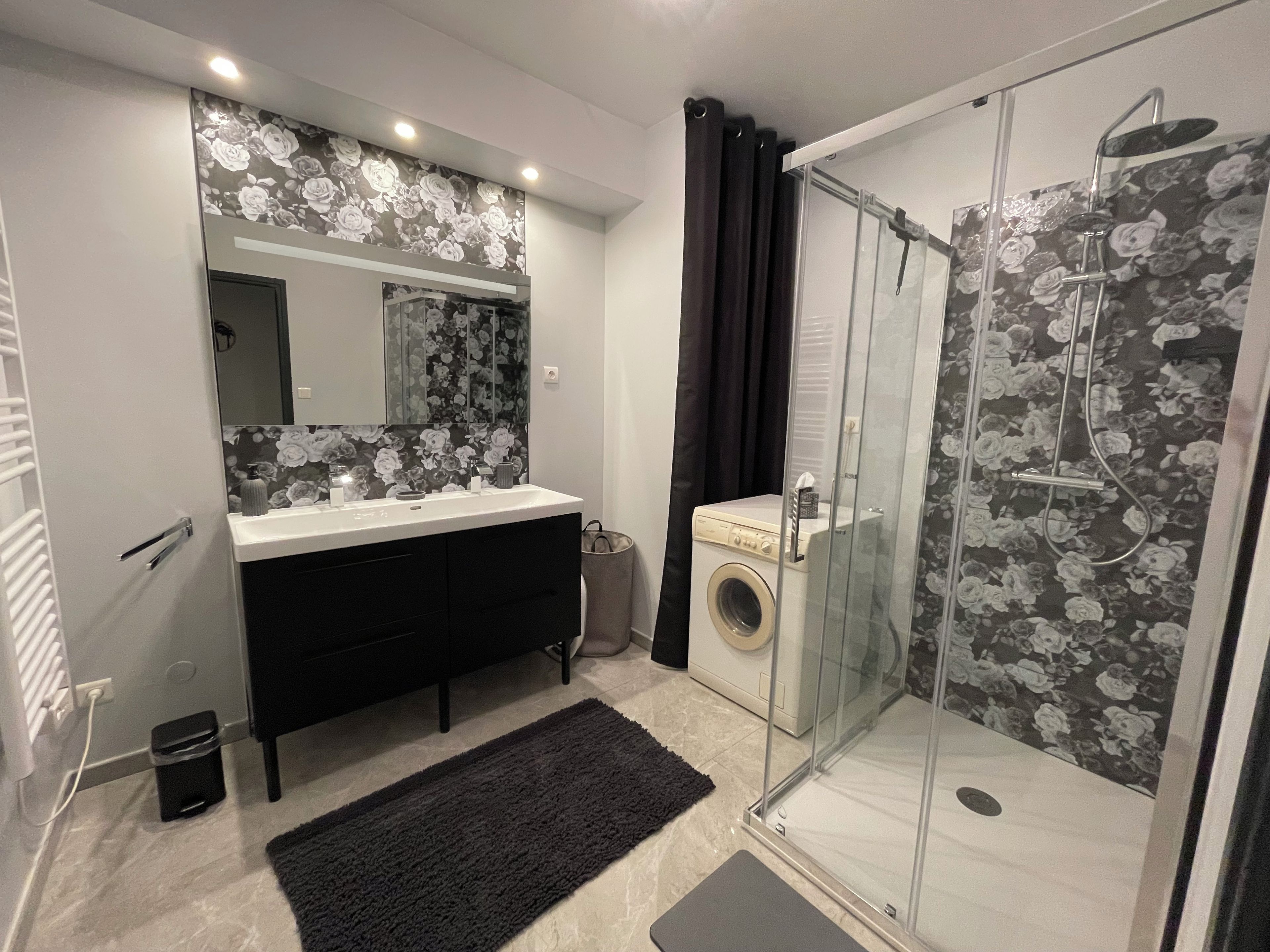 A bathroom with a shower, a washing machine, a sink, and a mirror.