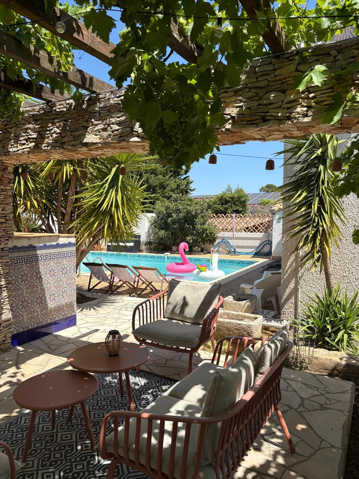 Zona de piscina con pared de piedra, piscina, sillones de descanso y flotador con forma de flamenco.