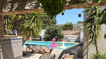 Zona de piscina con pared de piedra, piscina, sillones de descanso y flotador con forma de flamenco.