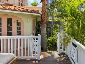 A wooden deck with a white railing, a palm tree, and a stone wall. - Palm Breeze Villa – Private Pool, Beach Club Access & Sugar Hill Resort (Porters)