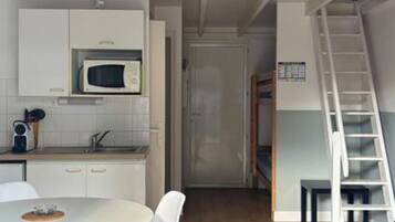 Una cocina compacta con gabinetes blancos, microondas y un pequeño comedor con mesa y sillas blancas.