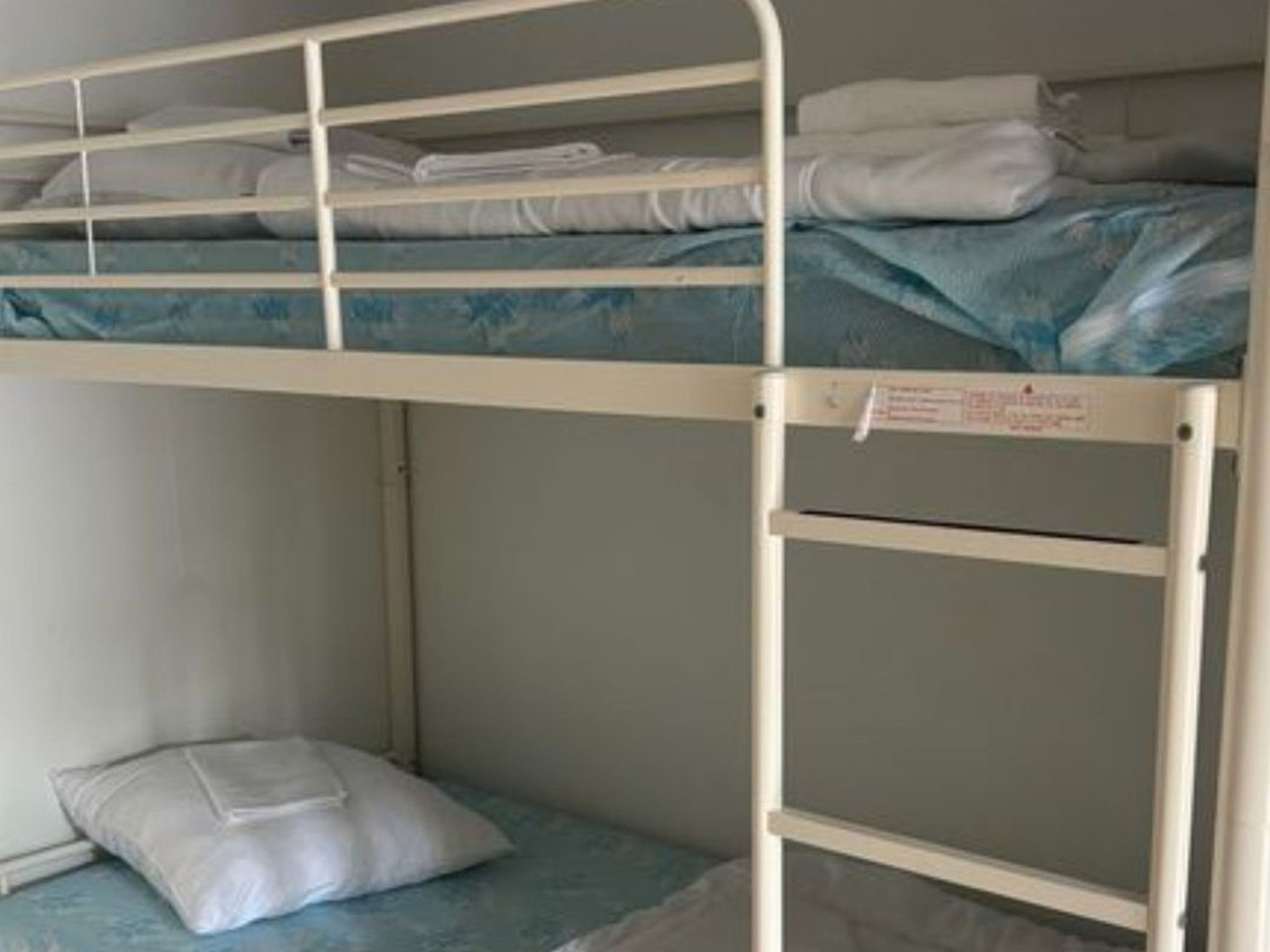 A bunk bed with a mattress and pillows, a white wall, and a door.