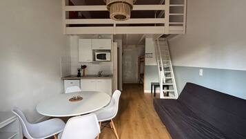 A compact living space with a kitchenette, a dining area, and a loft bedroom with a ladder.