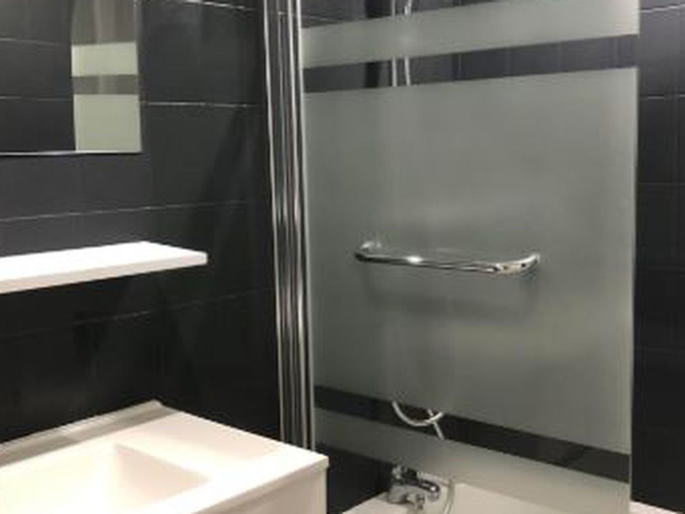 Ein modernes Badezimmer mit Duschkabine aus Glas, einem weißen Waschbecken und einem Spiegel darüber.