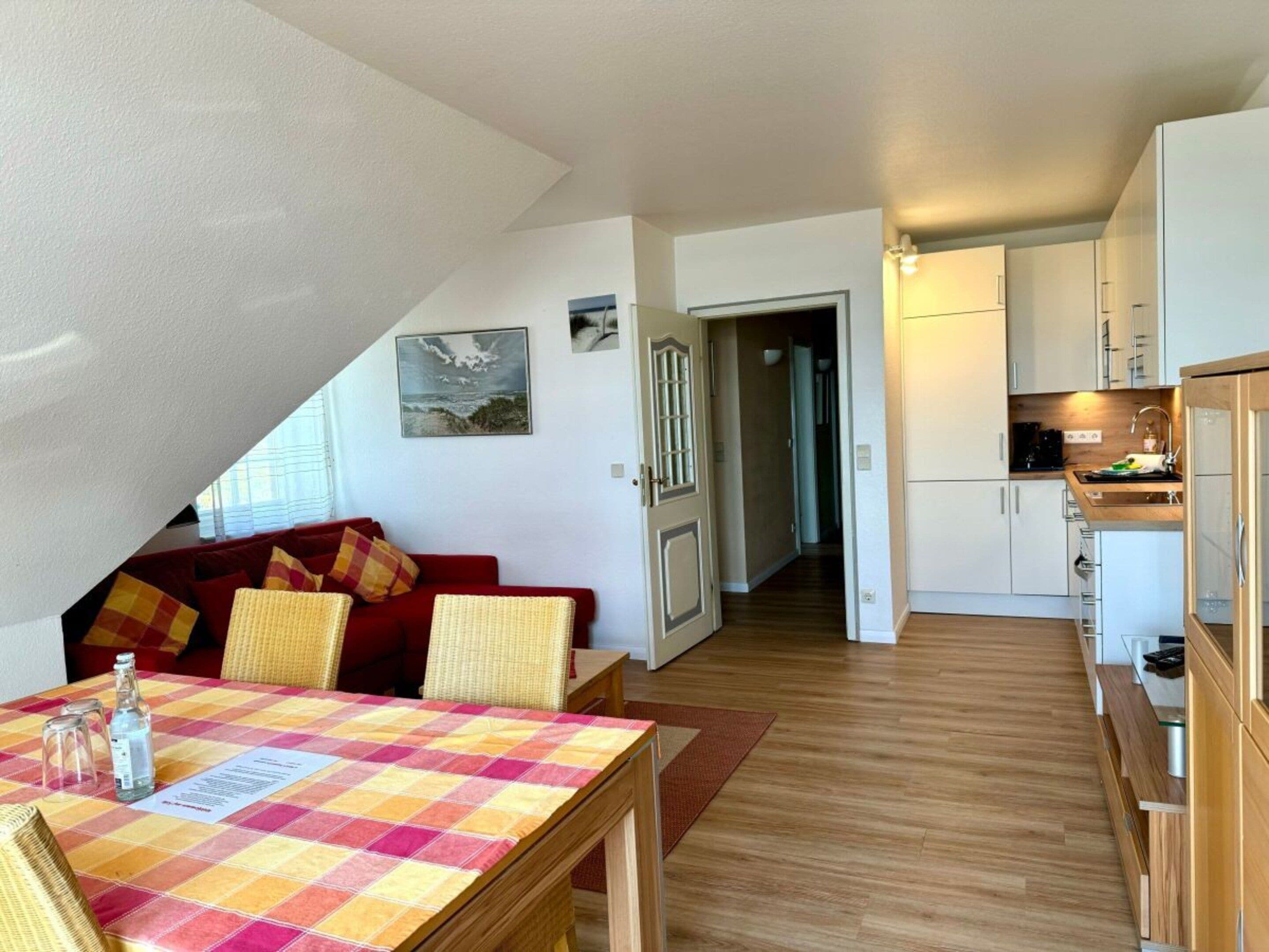Ein gemütlicher Wohnbereich mit einem roten Sofa, einem karierten Tisch und Blick zur Küche.