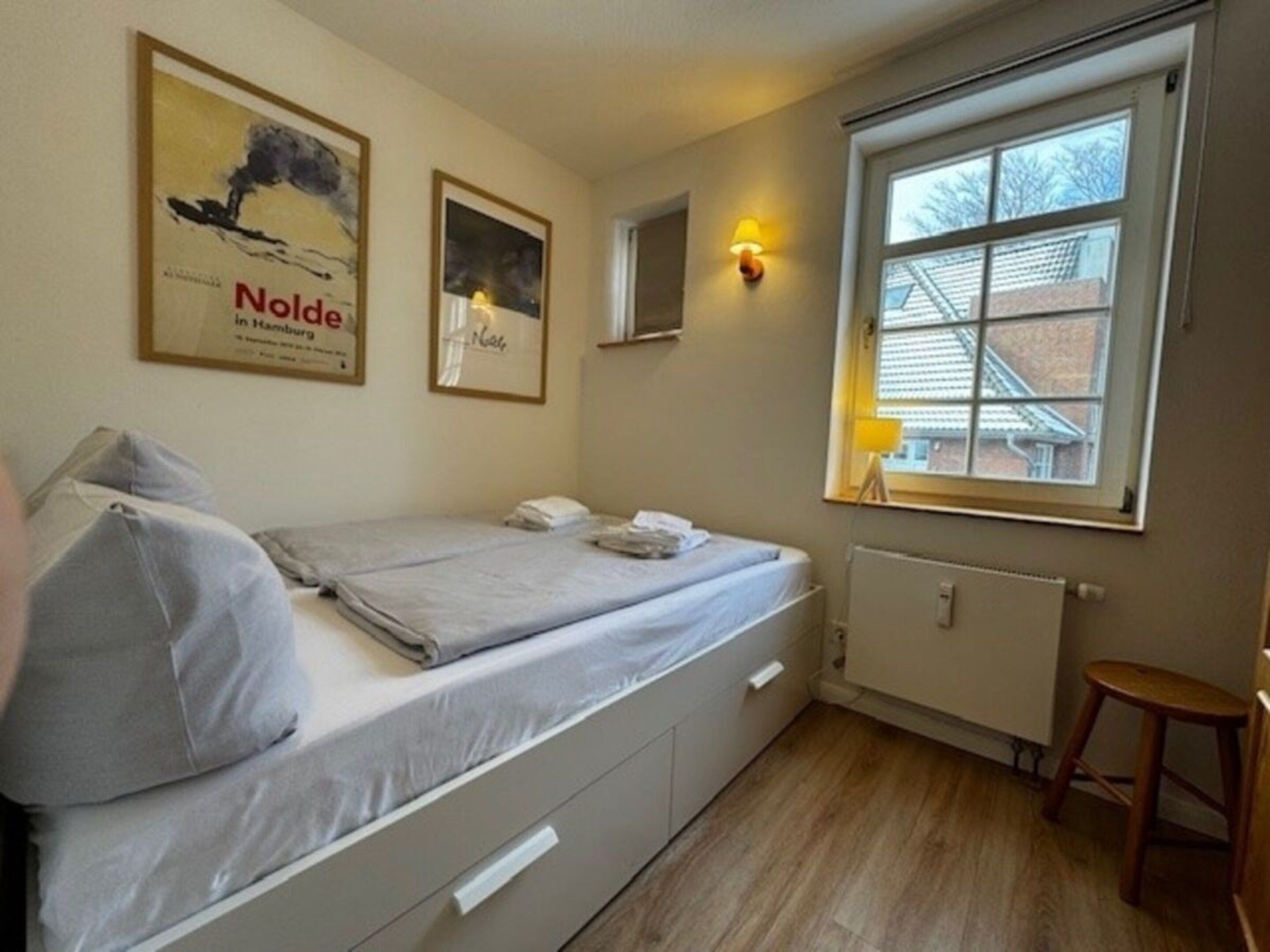 Ein Einzelzimmer mit Fenster, Heizkörper und Hocker.