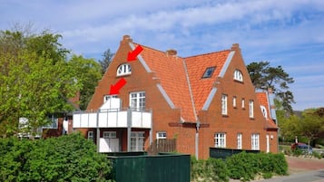 A two-story brick house with a sloped roof, a small window on the upper floor, and a green fence in the foreground.