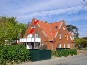 A two-story brick house with a sloped roof, a small window on the upper floor, and a green fence in the foreground. - "haus Parkstrasse" - Apt. 07 (Wyk auf Foehr)