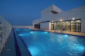 Een zwembad naast een gebouw met een modern ontwerp, met een heldere lucht en een rustig wateroppervlak.
