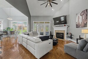 A modern living room with a white sofa, a grey armchair, a fireplace, a flat-screen TV, and a dining area with a table and chairs. - 5BR Masters Retreat ~ 10 min to Augusta National (Martinez)