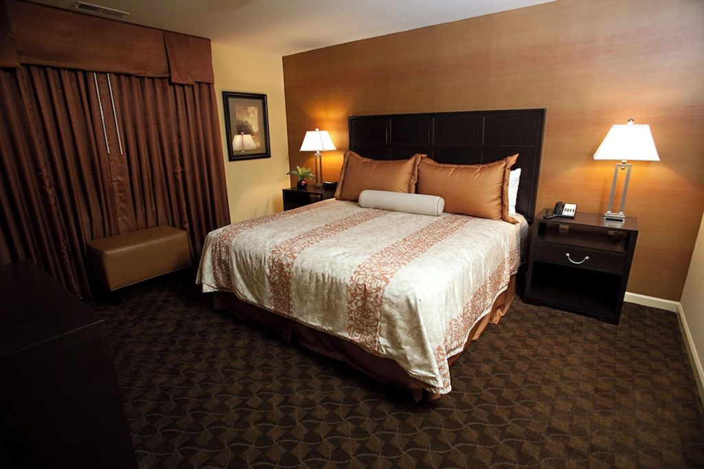 A hotel room with a large bed, two bedside tables with lamps, a bench, and a headboard.