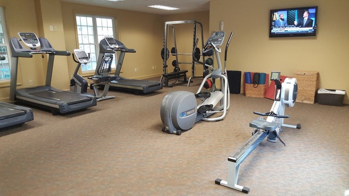 A gym with treadmills, an elliptical, a weight machine, and a television on the wall.