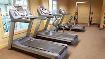 A gym with treadmills, a weight bench, and a window overlooking a pool.