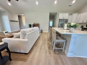 A modern kitchen with a central island, white cabinetry, and a dining area with a sofa and chairs. - Wonderful 4-bedroom house in adorable Pawleys Island (Pawleys Island)