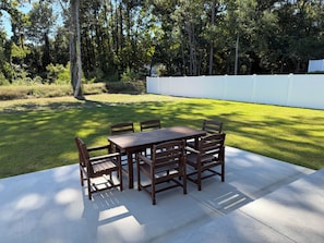 A patio with a table and chairs, surrounded by a well-maintained lawn and a white fence. - Wonderful 4-bedroom house in adorable Pawleys Island (Pawleys Island)