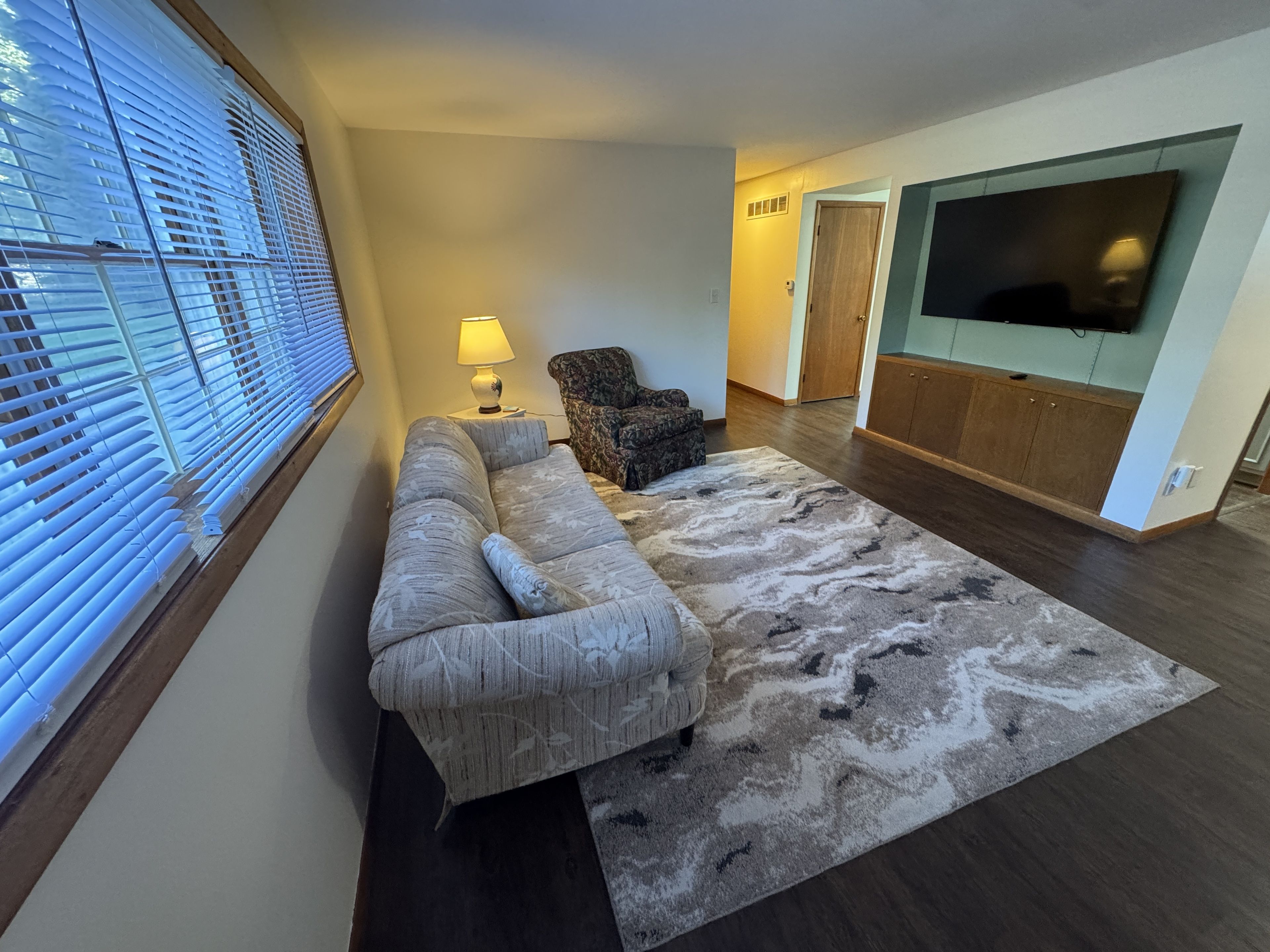 A living room with a sofa, a patterned rug, a lamp, a television, and a wooden cabinet.