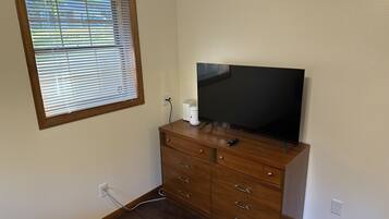 Una habitación con un aparador de madera, un televisor encima, una ventana con persianas y un enchufe en la pared.