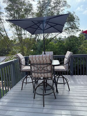 A deck with a table and chairs under a large umbrella, surrounded by a wooden deck and trees. - Beautiful 3BR Home in La Mesa\ Spacious & Comfortable (La Mesa)