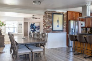 A spacious kitchen with a brick accent wall, a large dining table, and modern appliances. - Beautiful 3BR Home in La Mesa\ Spacious & Comfortable (La Mesa)