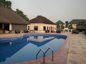 A swimming pool with lounge chairs and a building with a tiled roof. - Vanessa Paris Hotel (Owerri)