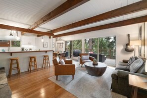 A spacious living area with a wooden ceiling, a kitchen with white cabinets, and a large window overlooking greenery. - Tahoe Retreat with Hot Tub in Carnelian Bay (Carnelian Bay)
