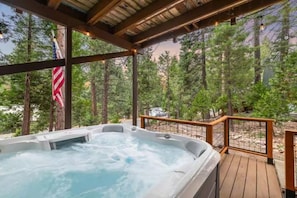 Ein Whirlpool auf einer Holzterrasse mit Blick auf einen Wald.
