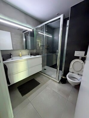 A modern bathroom with a glass-enclosed shower, a white toilet, and a vanity with a mirror. - Short Stay Experts A3 - E1 Studio  8 floor apartment (Gibraltar)