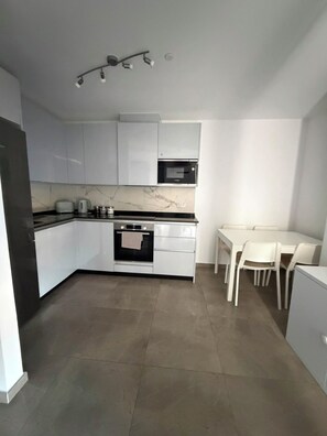 A modern kitchen with white cabinets, a built-in oven, and a dining area with a table and chairs. - Short Stay Experts A3 - E1 Studio  8 floor apartment (Gibraltar)