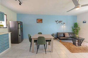 Een moderne keuken met een koelkast, een eettafel met stoelen, een bank en een kleine tafel met een lamp.