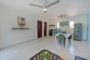 A spacious living area with a dining table, chairs, a ceiling fan, and a kitchen area with cabinets and appliances. - Modern Sosua APT Near Beaches and Cafe (Sosúa)