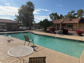 A clear swimming pool with lounge chairs and a table, surrounded by a fenced patio area with palm trees and shrubs. - Modern 3-bedroom & 2-bathroom townhome in Phoenix (Phoenix)