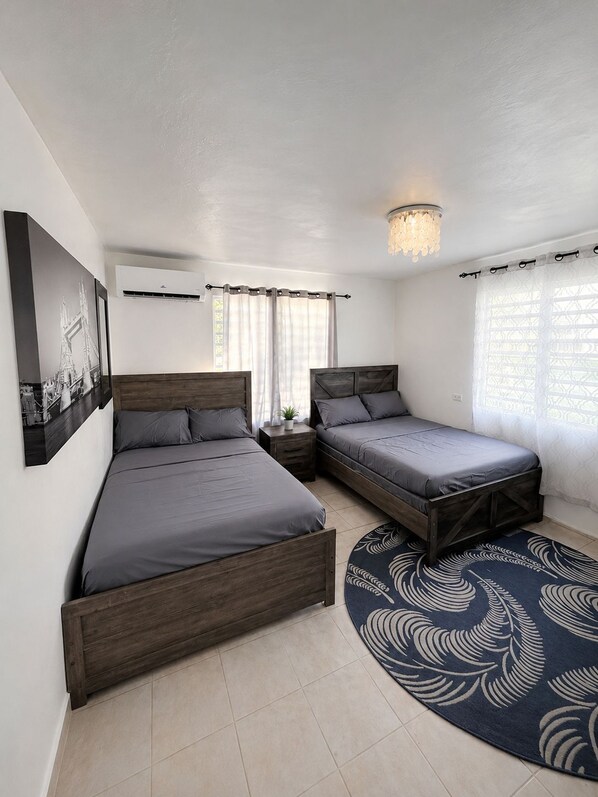 Una habitación con dos camas, un tapete redondo, una lámpara de techo y un aire acondicionado de pared.