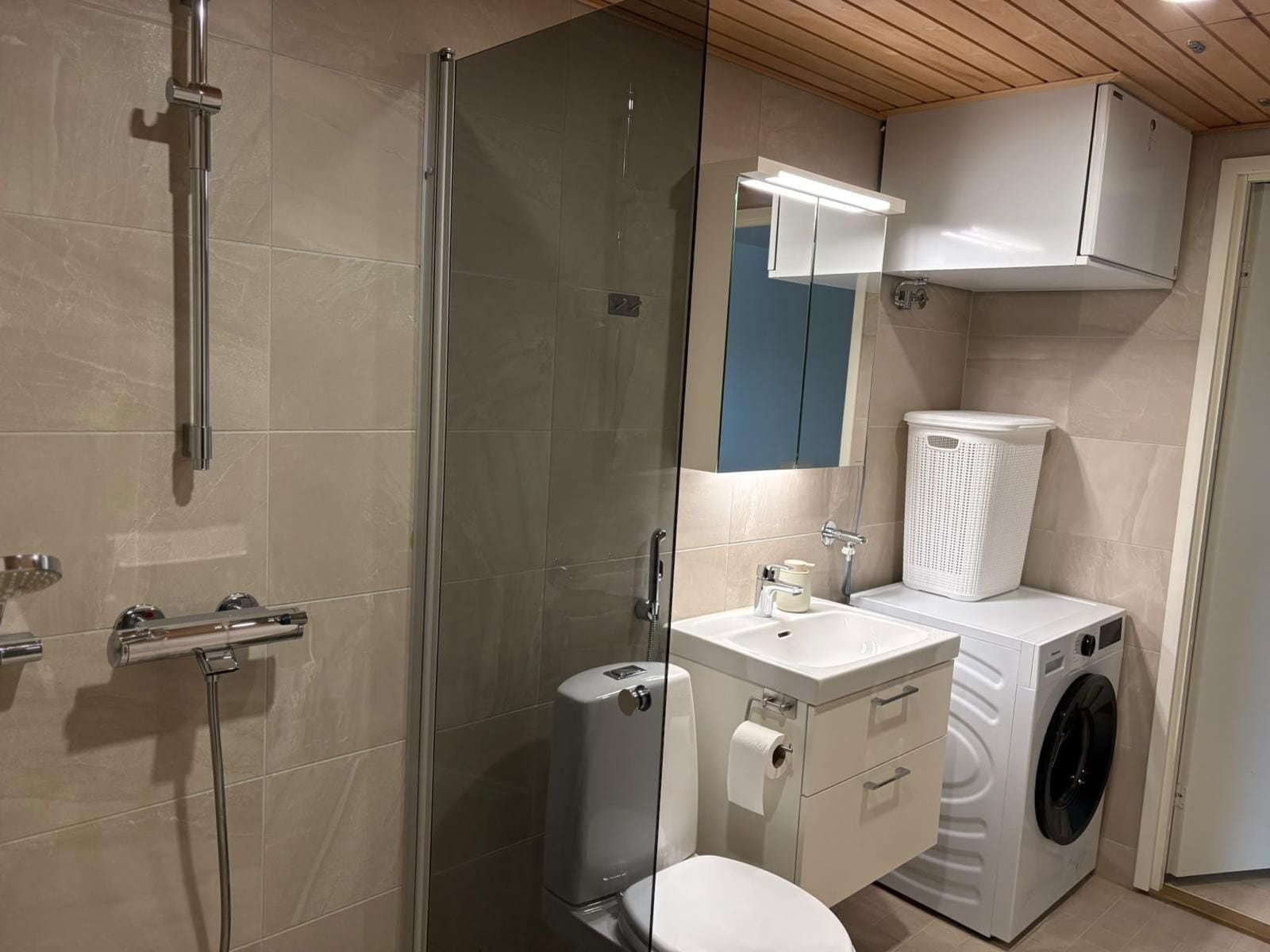 A compact bathroom with a glass-enclosed shower, a toilet, a sink with a mirror, and a washing machine.