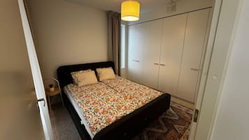 A bedroom with a bed, wardrobe, and a hanging light fixture.