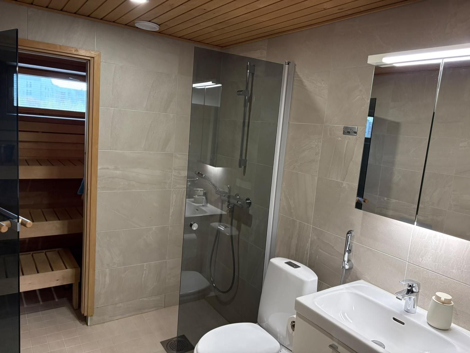 A modern bathroom with a glass-enclosed shower, a white toilet, and a sink with a mirror above it.