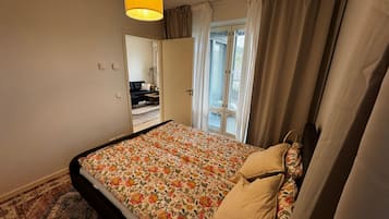 Ett sovrum med en säng, ett fönster med gardiner, en dörr och en hängande lampa.
