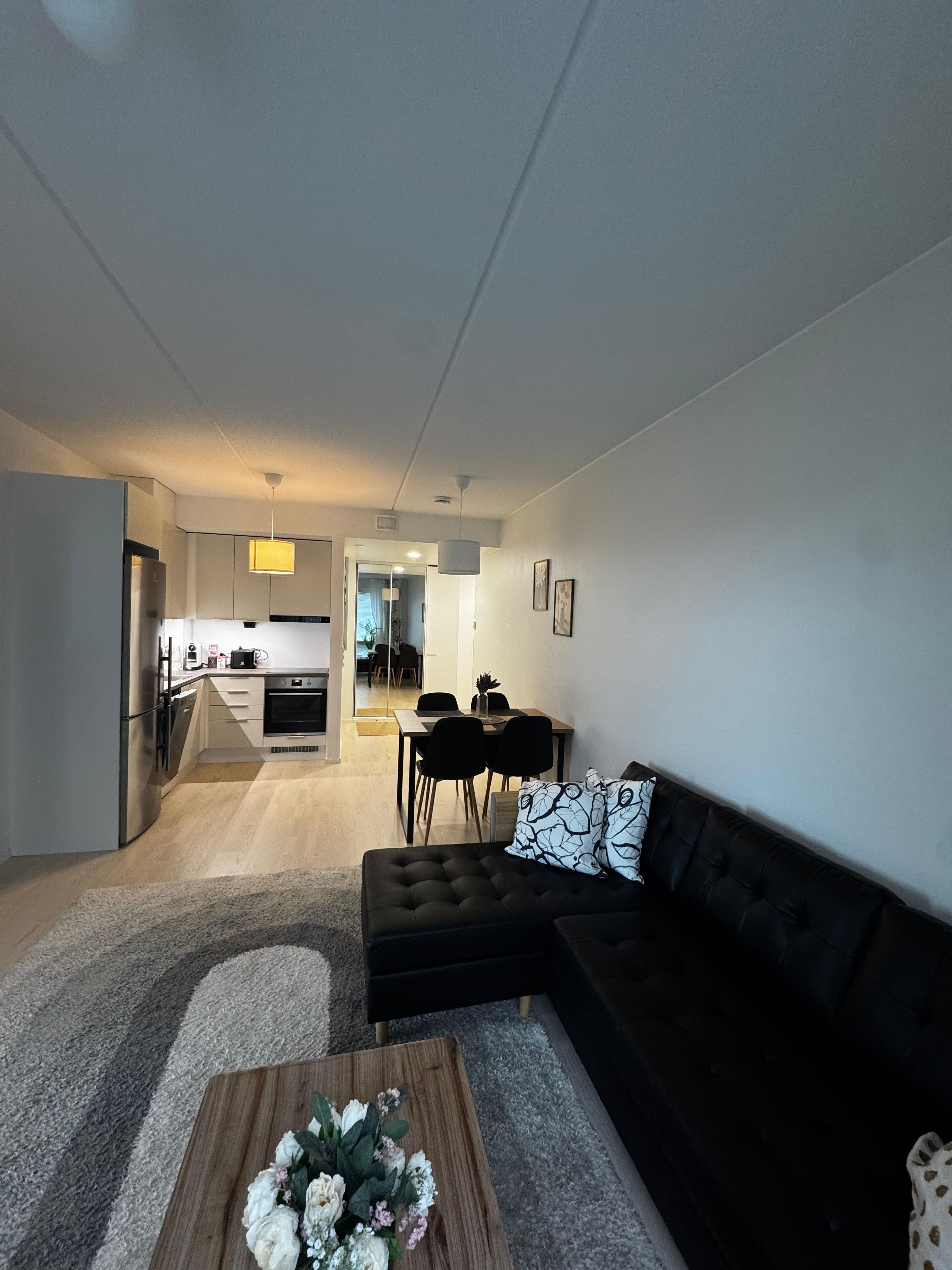 Ein modernes Wohnzimmer mit einer schwarzen Couch, einem Holztisch und einem Essbereich im Hintergrund.