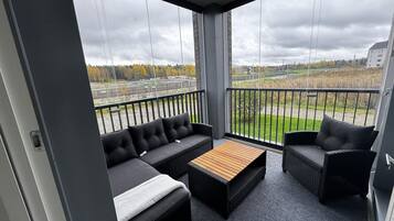 Een balkon met een bank, een klein tafeltje en rieten stoelen.