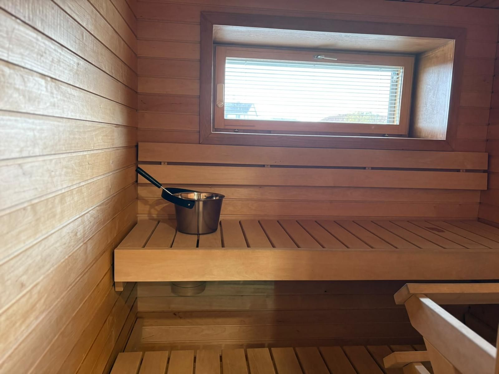 Un espai de sauna amb parets de fusta, una finestra i un cubell metàl·lic.