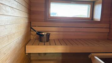 Un espai de sauna amb parets de fusta, una finestra i un cubell metàl·lic.