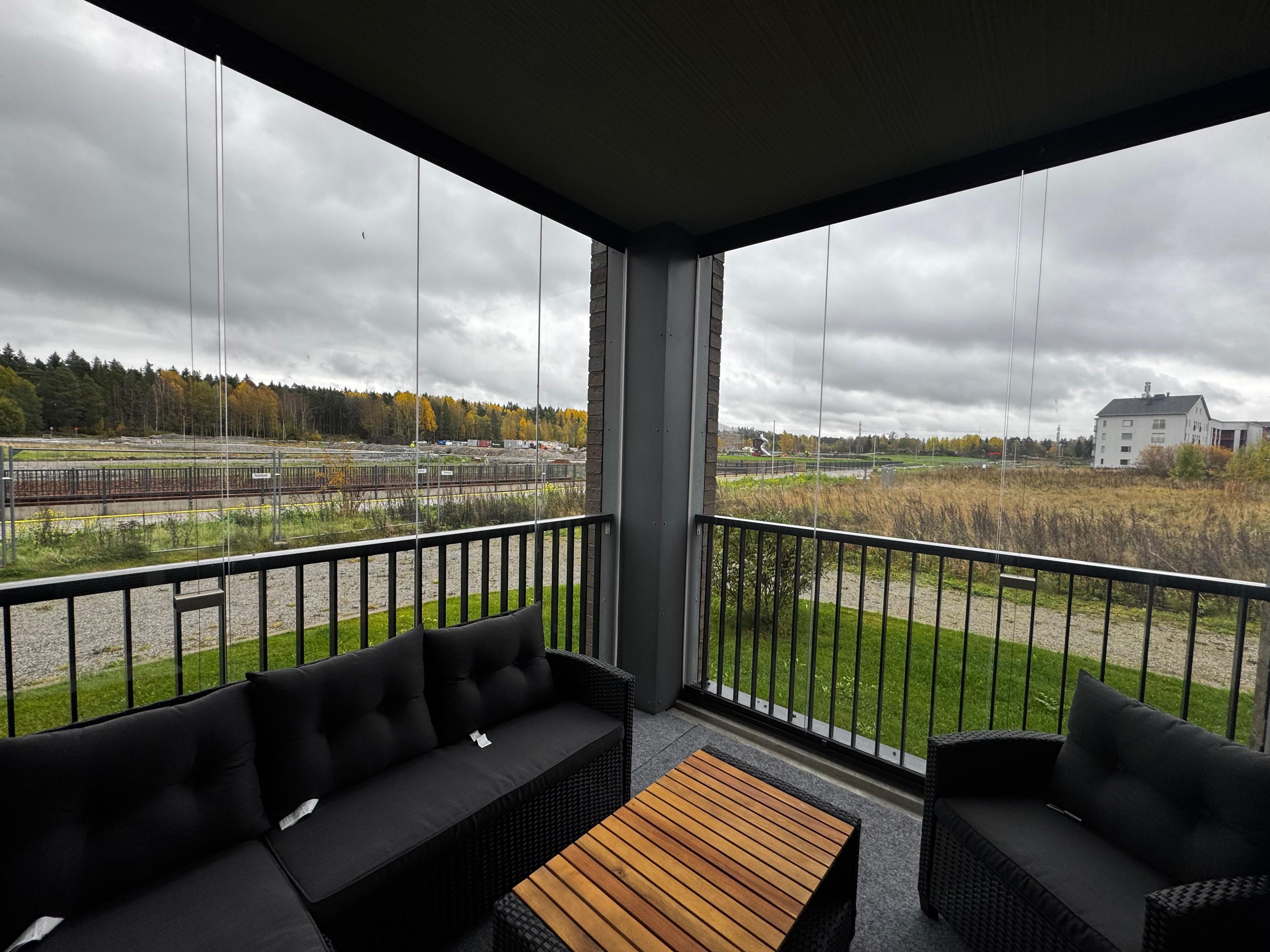 Ein Balkon mit einer Couch und einem kleinen Tisch, mit Blick auf Gleise und ein Gebäude.