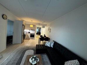 Un saló modern amb un sofà negre, una taula de centre amb flors, i una zona de menjador amb taula i cadires.