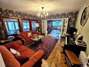 Uma sala de estar com um sofá vermelho, uma mesa de centro, um piano e uma estante de livros.