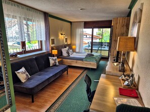 A hotel room with a sofa, a bed with a wooden headboard, a desk with a lamp, and a view of the outside. - Landhotel Schönblick Group House for up to 47 people (Bad Herrenalb-Rotensol)