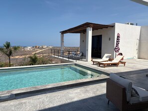 En swimmingpool med solstolar och en pergola med utsikt över ett kustlandskap.